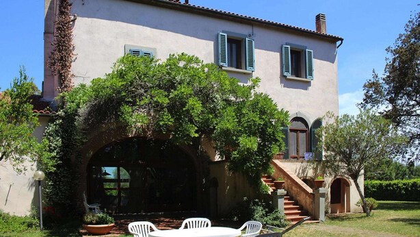 Una casa de dos pisos con un porche cubierto, una escalera que conduce al nivel superior y un jardín con mesa y sillas.
