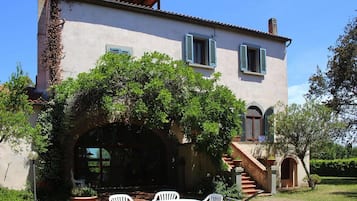 A two-story house with a covered patio, a staircase leading to the upper floor, and a garden area with a table and chairs.