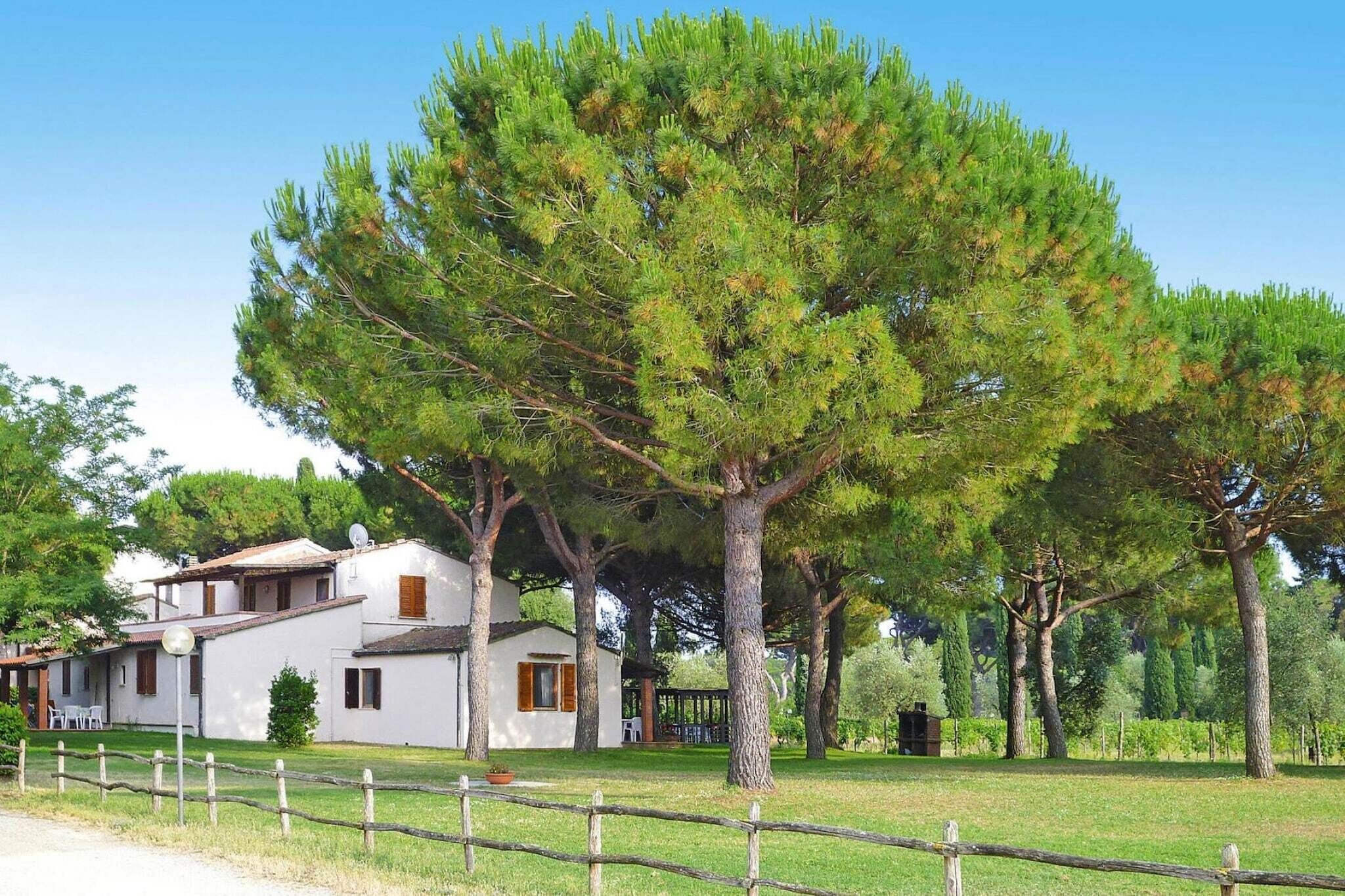 A white building with a satellite dish, surrounded by a wooden fence and large trees.