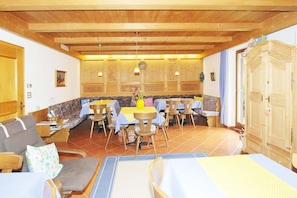A dining area with wooden tables and chairs, a sofa, and a kitchen area with wooden cabinets. - Apartment in Latsch with Indoor Pool & Garden (Latsch)
