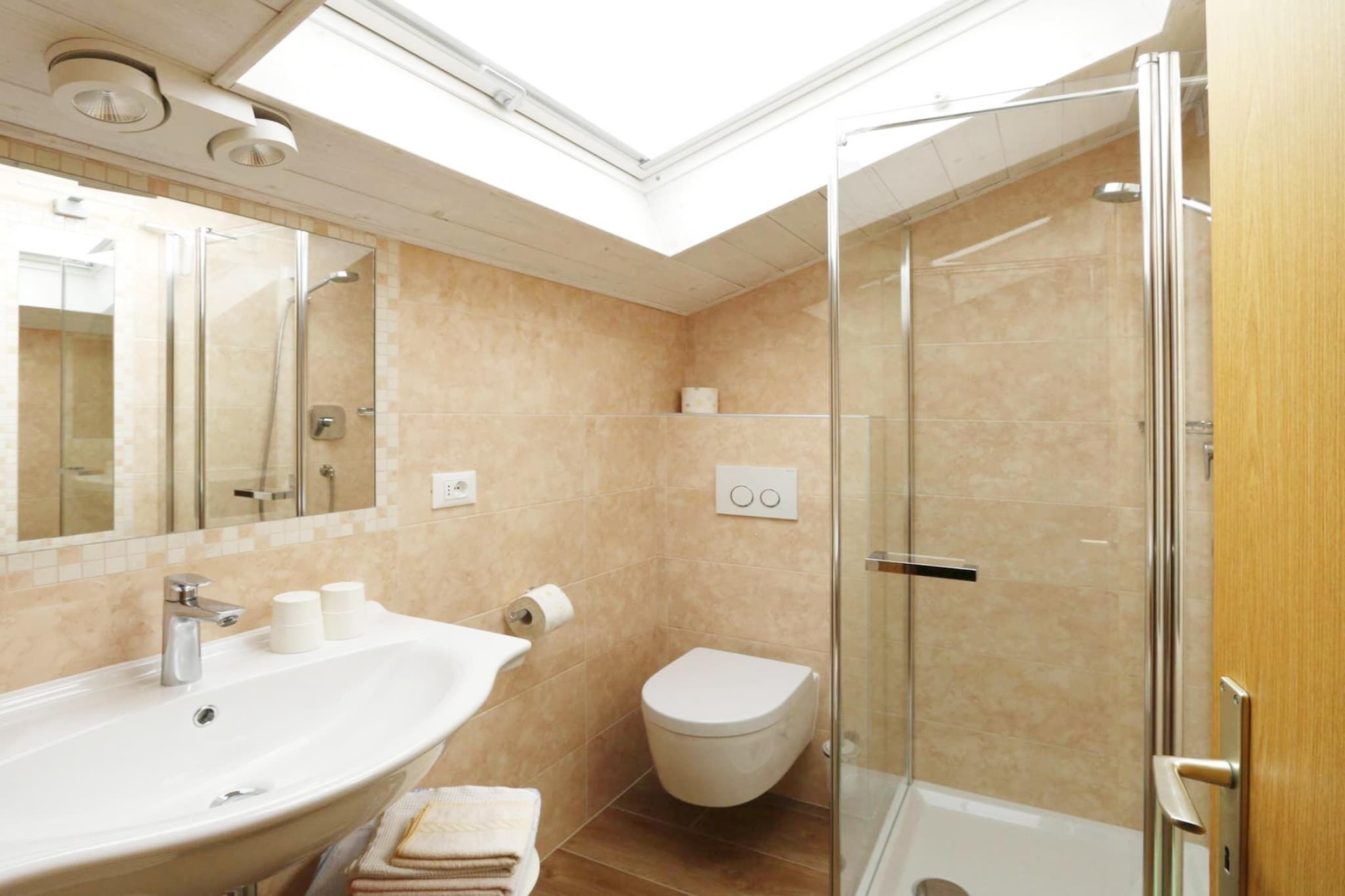 Une salle de bain dotée d’un puits de lumière, d’un lavabo, de toilettes et d’une douche à parois de verre.