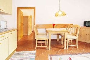 Un comedor con una mesa y sillas de madera, una lámpara colgante, y una zona de cocina con armarios y una cafetera.