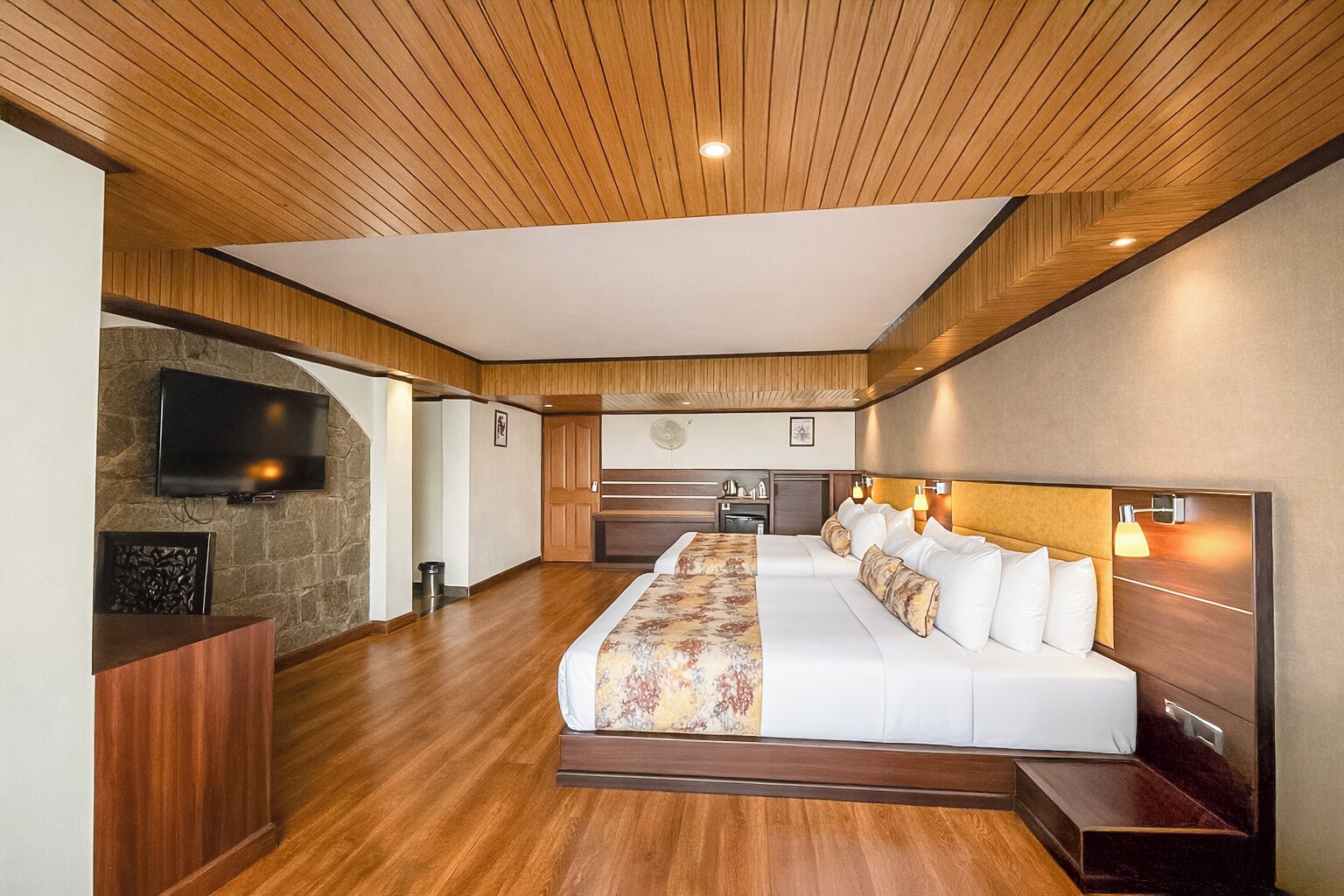 A hotel room with a large bed, a TV mounted on the wall, a desk, and a stone accent wall.