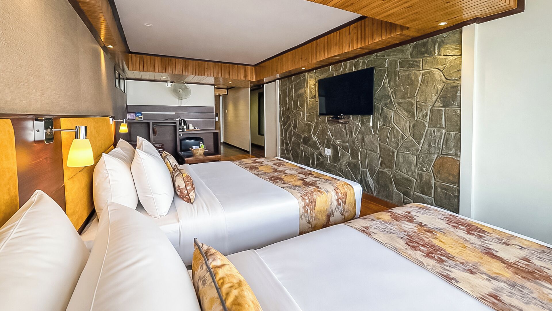 Een hotelkamer met twee bedden, een stenen muur, een flatscreen televisie en een kitchenette.