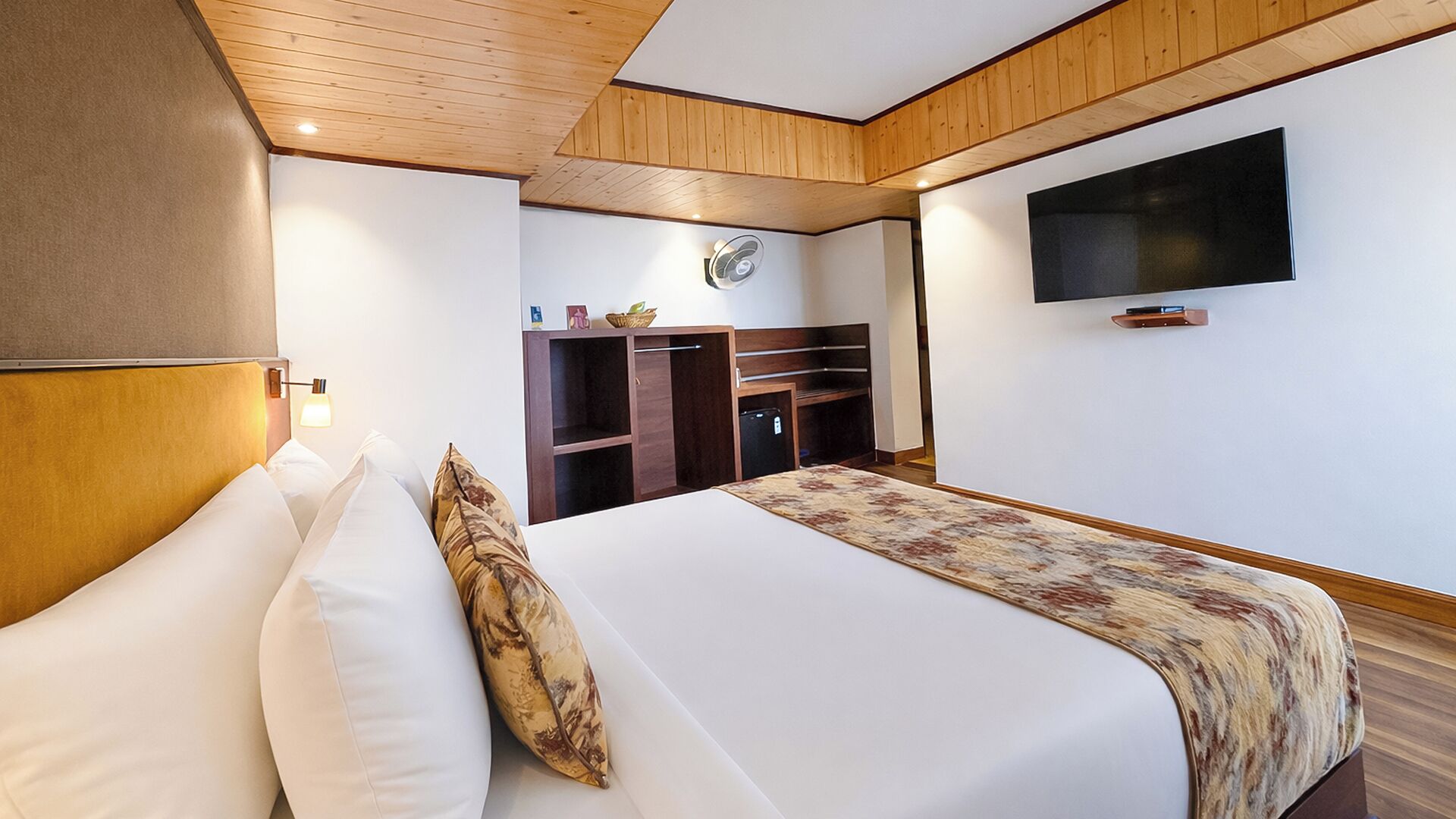 Een hotelkamer met een bed, een aan de muur bevestigde televisie en een houten plafond.