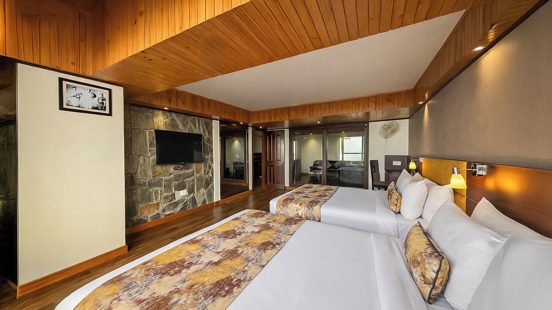 Een moderne hotelkamer met een groot bed, een wand van natuursteen, een flatscreen televisie en een houten plafond.