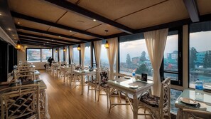 Un restaurante con mobiliario de mimbre, amplios ventanales y vistas a la ciudad.