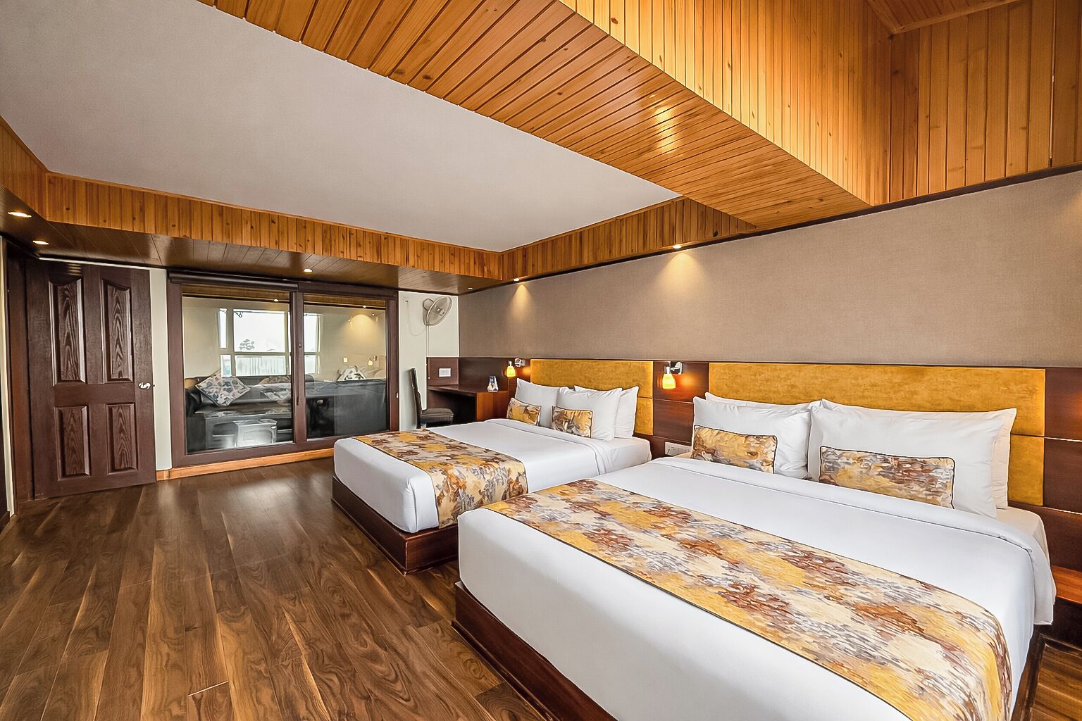 Habitación de hotel con dos camas, piso de madera, puerta corrediza de vidrio a un balcón y un diseño moderno en el techo.
