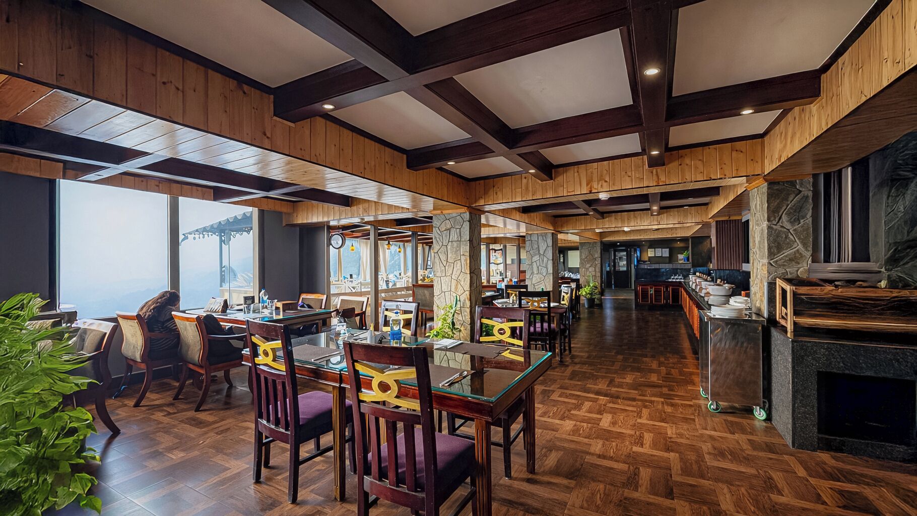 A restaurant with wooden floors, high ceilings, and large windows offering views of the outdoors.