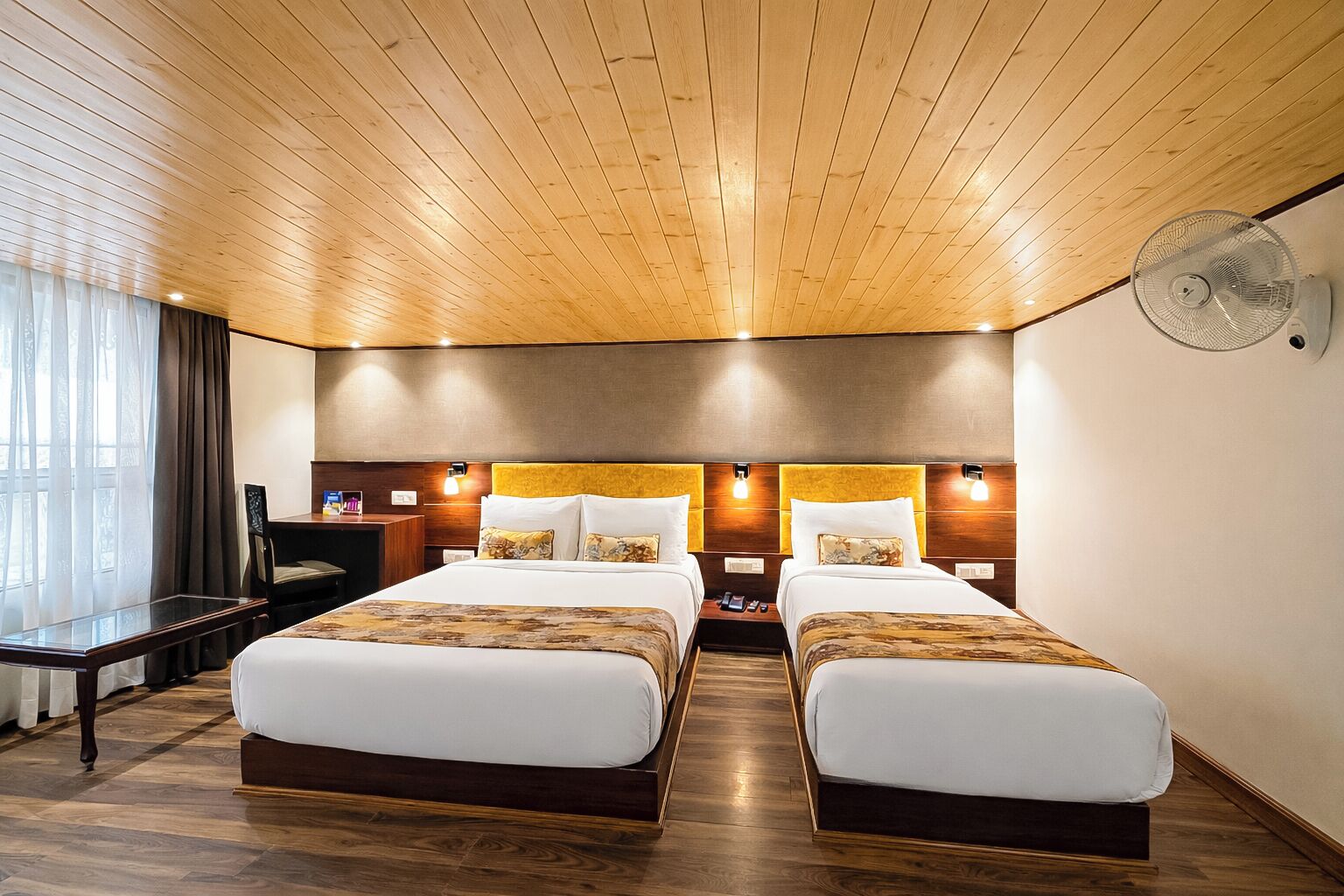 Een hotelkamer met twee bedden, een houten plafond en een bureau met een stoel.