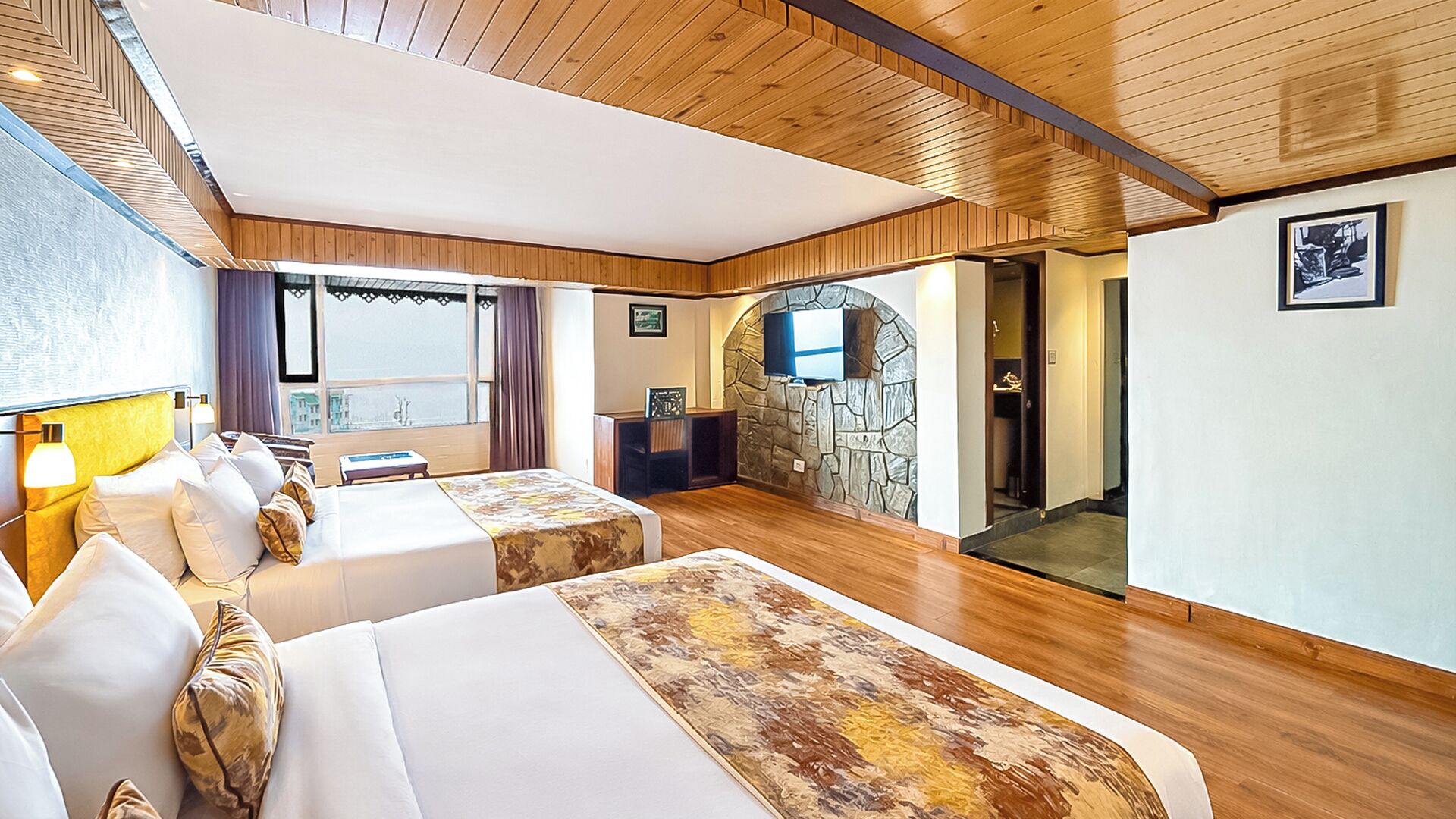 Habitación de hotel con dos camas, una pared de piedra, televisión y vista al mar.