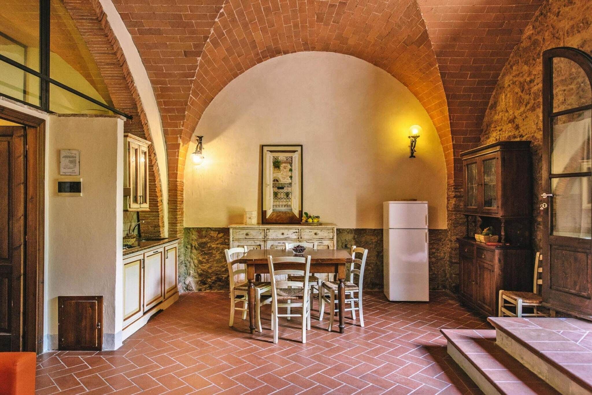 Una cucina rustica con un arco in mattoni, mobili in legno, un tavolo da pranzo con sedie e un frigorifero.