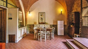 A rustic kitchen with a brick arch, wooden cabinets, a dining table with chairs, and a refrigerator.
