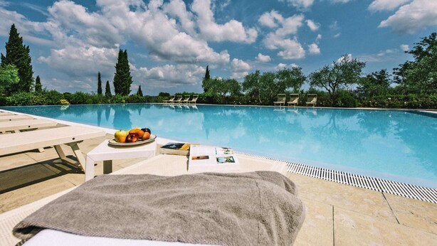 A poolside area with lounge chairs, a table with fruits and magazines, and a clear blue sky.