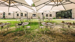 An outdoor dining area with tables and chairs under large umbrellas, surrounded by stone buildings.
