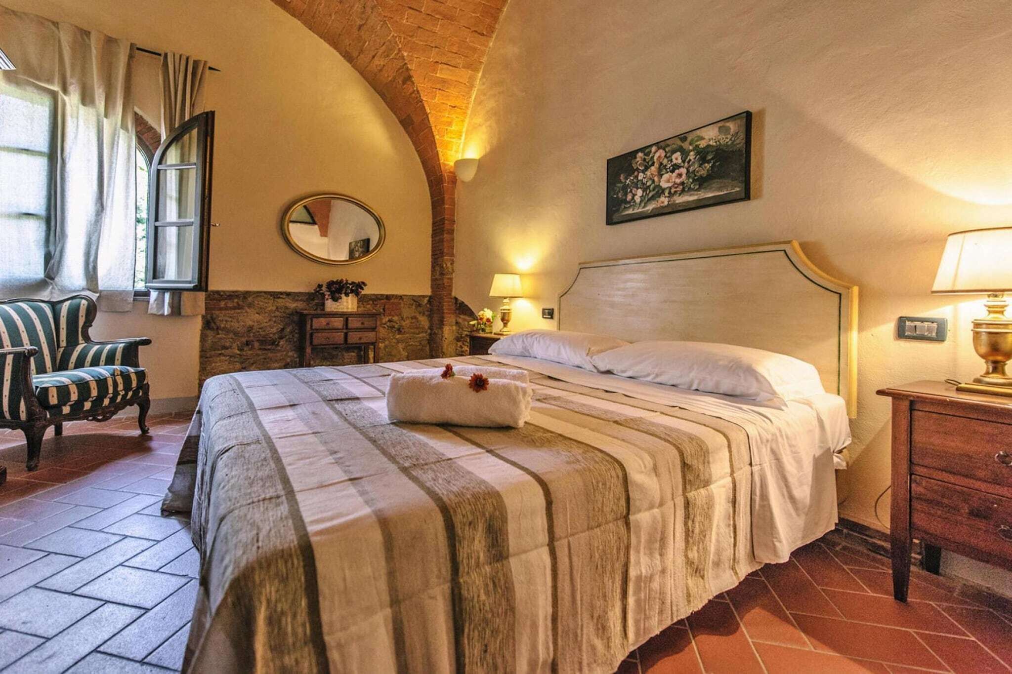 Un dormitorio acogedor con una cama grande, una silla, una mesita de noche, un espejo y un cuadro en la pared.