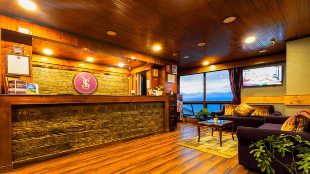 A reception area with a wooden reception desk, a stone wall, and a large window offering a view of the mountains. - Sumitel Hotel 500 meters from Mall Road (Darjeeling)