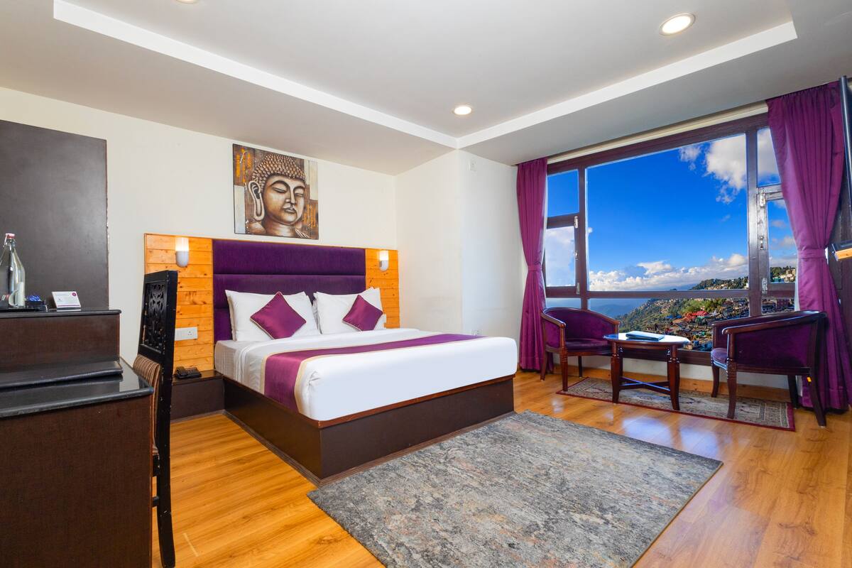 A modern hotel room with a large bed, a desk, and a view of the city.