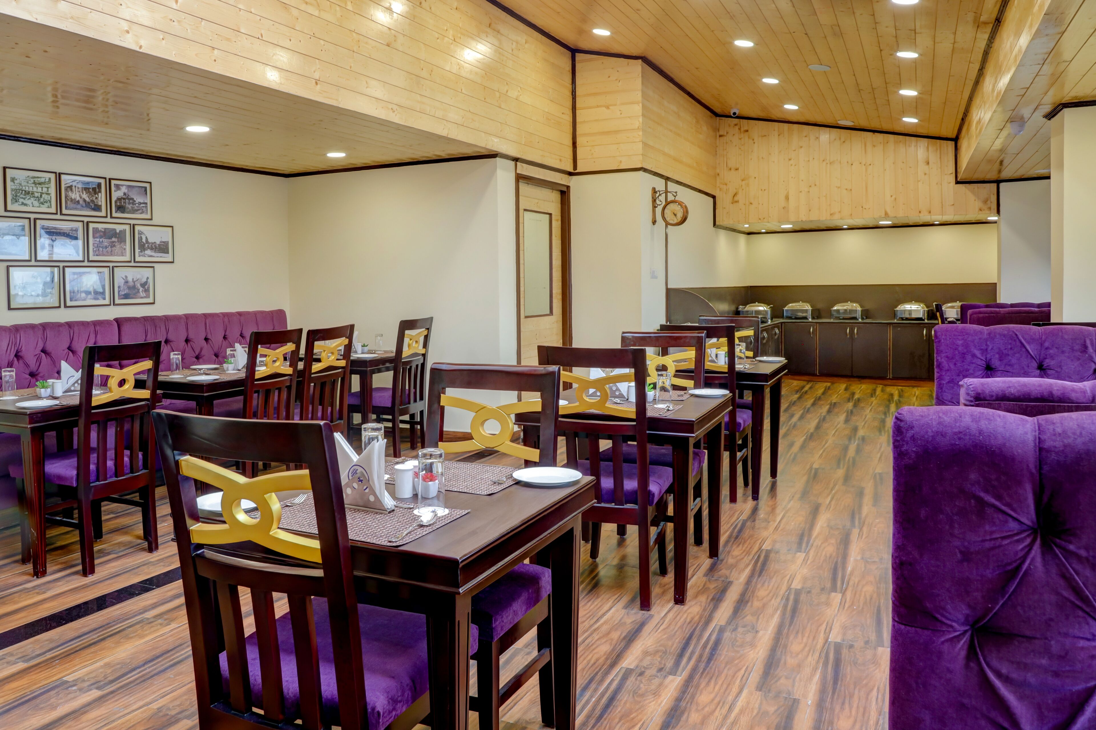 Un restaurante con techo de madera, asientos acolchados color púrpura y mesas de madera con sillas amarillas.