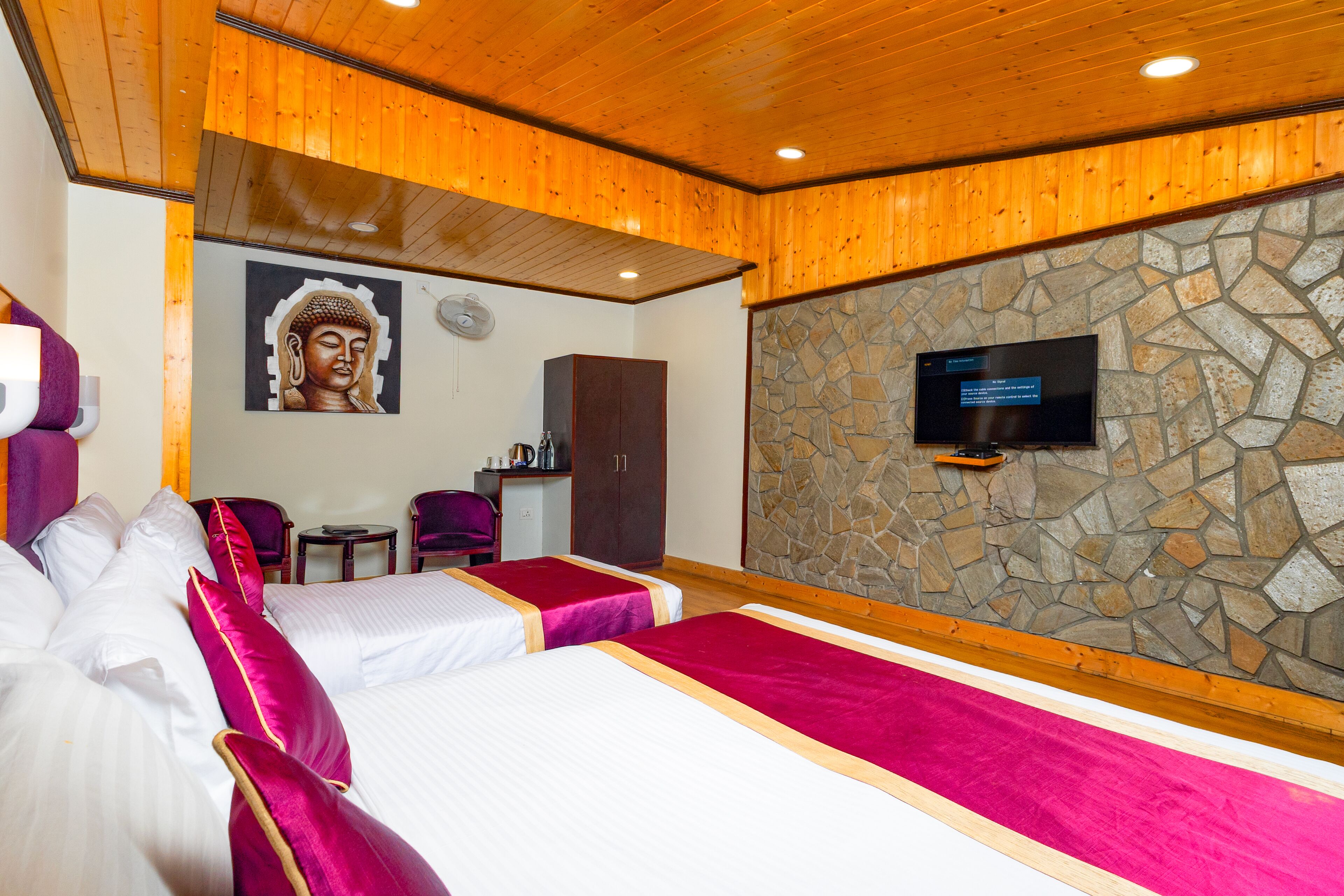A hotel room with two beds, a stone wall, a television, and a Buddha painting.