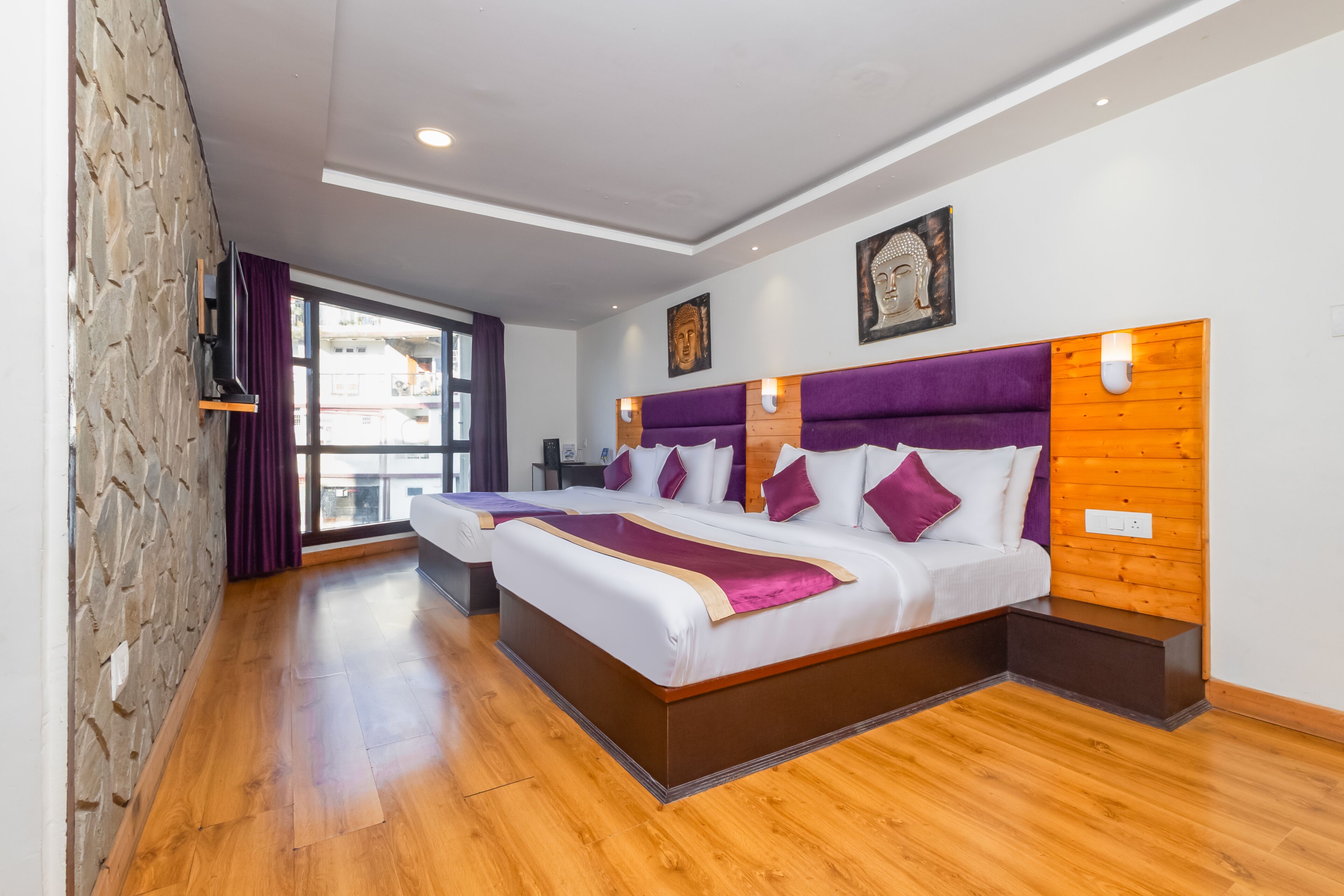 A modern hotel room with a large bed, a stone wall, and a view of the city.