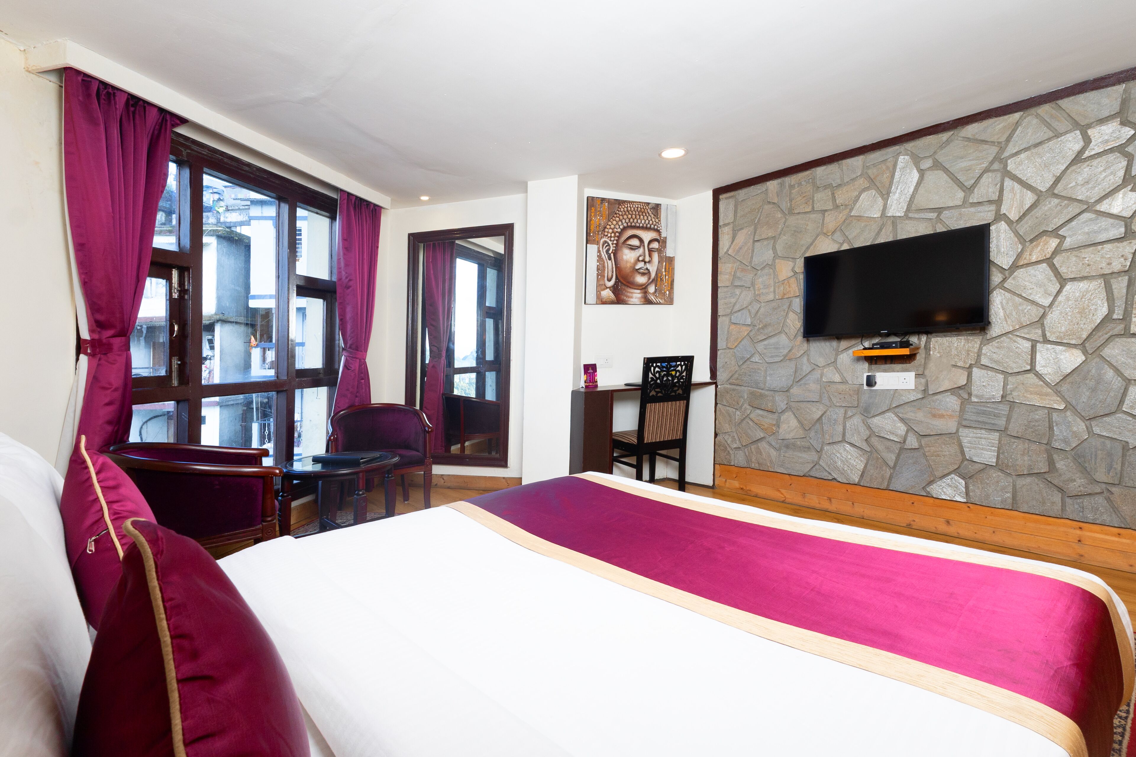 A hotel room with a large bed, a desk, a chair, and a TV mounted on a stone wall.