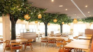 Un restaurante con mesas y sillas redondas, plantas de interior y luces colgantes.