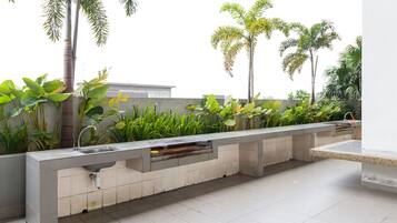 An outdoor kitchen area with a built-in sink and countertop, surrounded by lush greenery and palm trees.