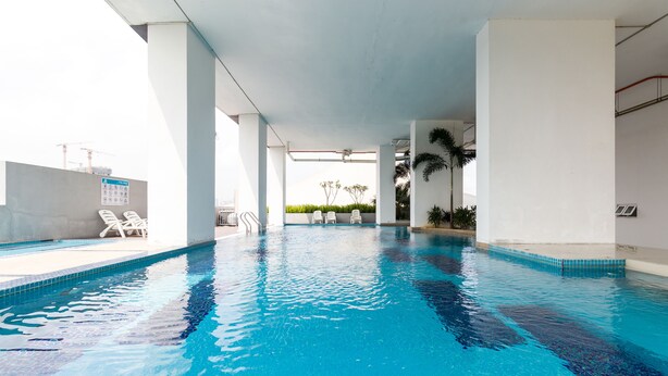 An indoor swimming pool with clear blue water, white poolside chairs, and a view of the city skyline in the background. - Boulevard Service Apartment KL by Airhost (Kuala Lumpur)
