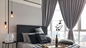 A modern bedroom with a black and white patterned bedspread, a pillow with text, a bedside table with a lamp, and a window with curtains. - Boulevard Service Apartment KL by Airhost (Kuala Lumpur)