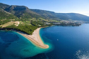 Vue aérienne d’une zone côtière avec une plage, des eaux cristallines et un paysage montagneux.