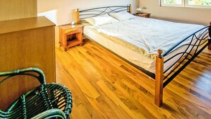 A bedroom with a wooden floor, a metal bed frame, a bedside table with a lamp, and a window with a view.