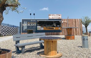 A food truck named Krokant with a menu board, a wooden bench, and a small table in a gravel area.