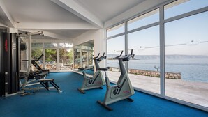 Un gimnasio con equipo de cardio y amplias ventanas con vistas a un cuerpo de agua.