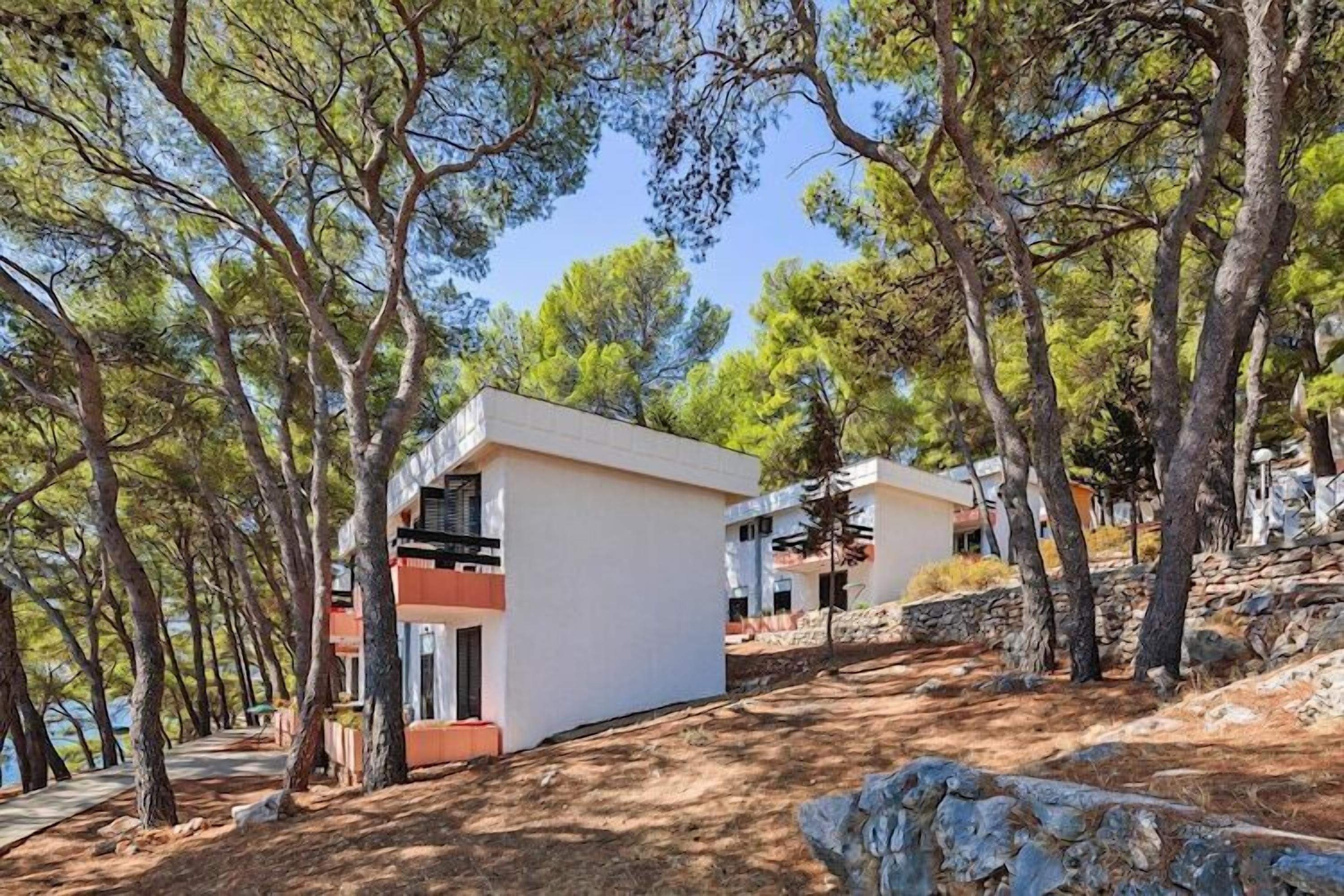 A modern building with a flat roof, surrounded by trees and rocky terrain.