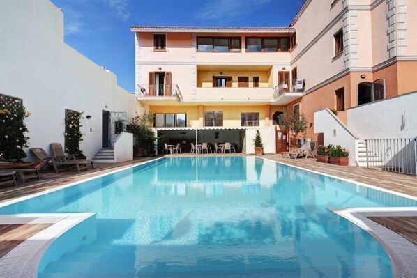 Una piscina con sillones de descanso y un edificio con balcones.