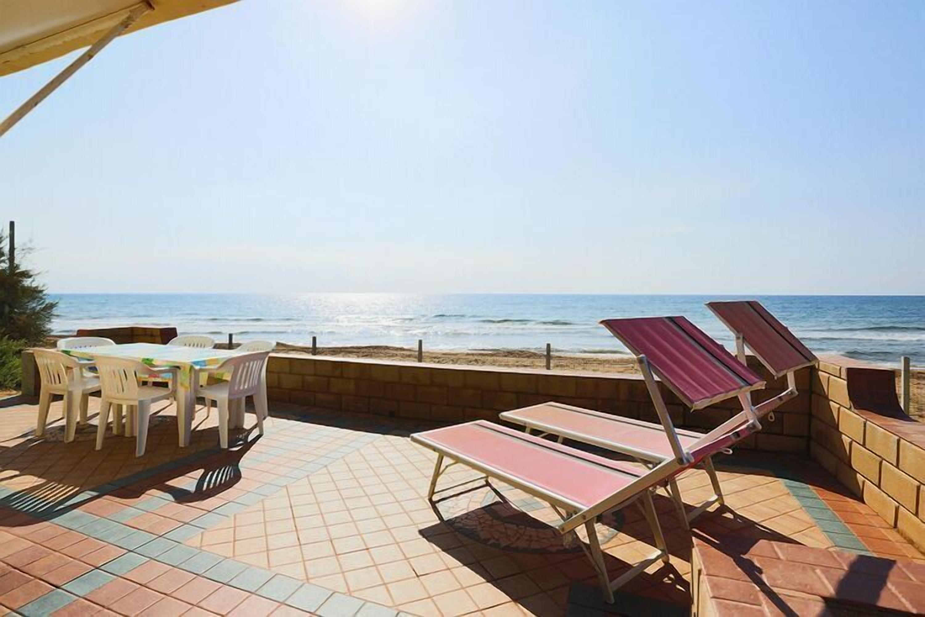 A patio with a table and chairs, a sun lounger, and a view of the ocean.