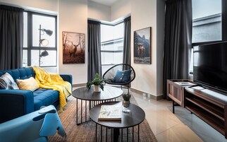 A modern living room with a blue sofa, a black chair, a coffee table with a book, and a TV on a wooden stand.