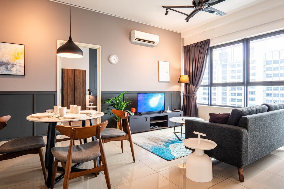 A modern living room with a sofa, dining table, chairs, a TV, and a large window with curtains.