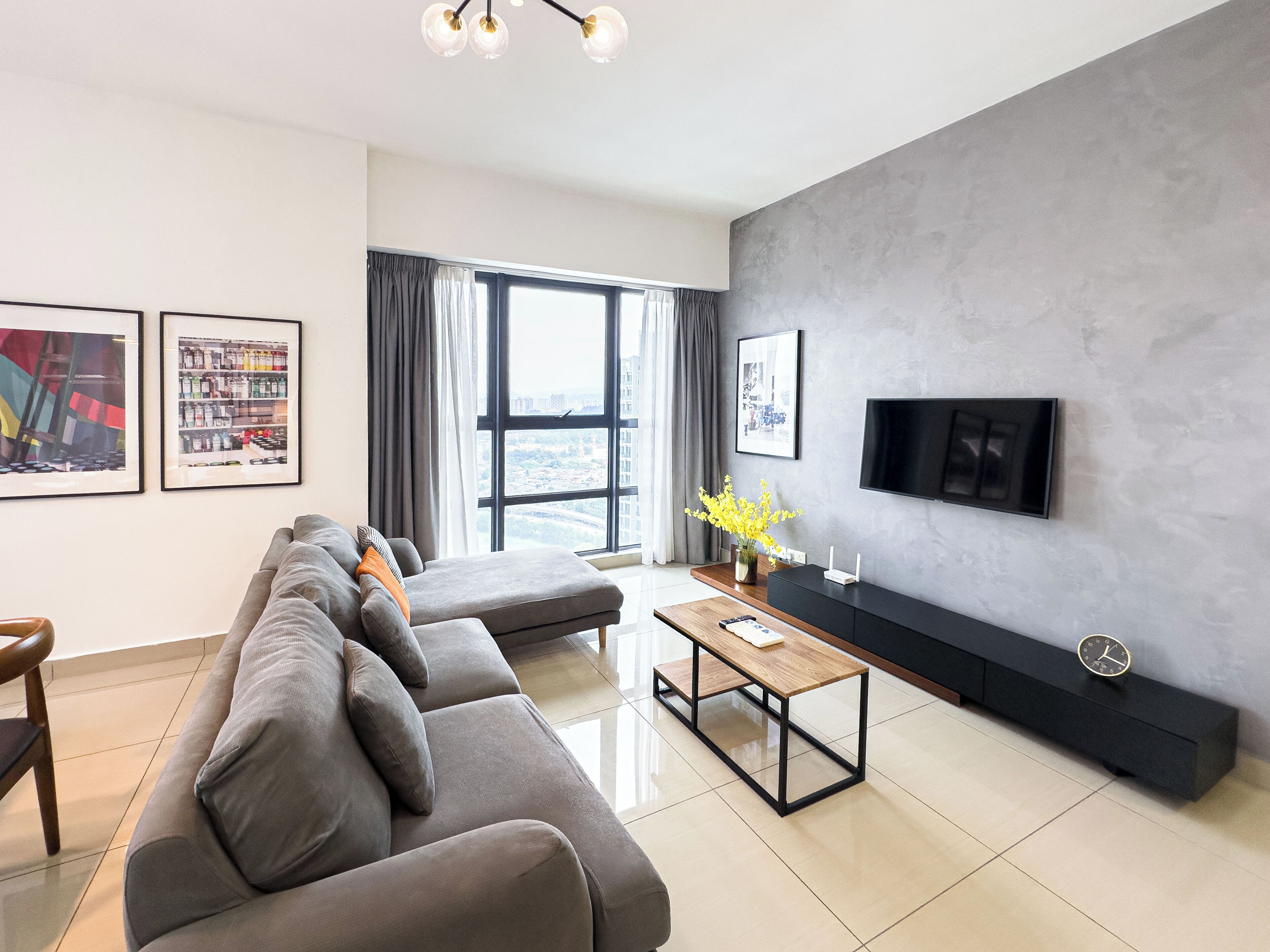 A modern living room with a grey sofa, a wooden coffee table, a flat-screen TV mounted on a grey wall, and a large window with curtains.