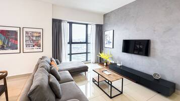 A modern living room with a grey sofa, a wooden coffee table, a flat-screen TV mounted on a grey wall, and a large window with curtains.