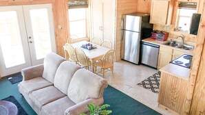 Una cabaña de madera compacta con comedor, kitchenette y sala de estar con sofá y una planta.