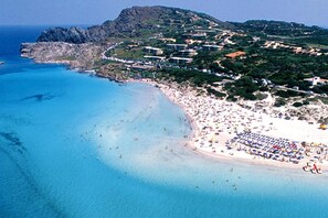 An aerial view of a coastal town with a large beach, clear blue waters, and buildings along the coastline.