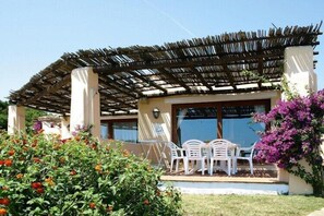 Un espace extérieur abrité, avec une pergola, des chaises en plastique blanches et une table.