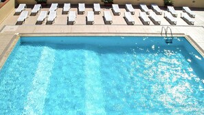 Une piscine rectangulaire à l’eau d’un bleu cristallin, entourée de chaises longues et d’une terrasse carrelée.