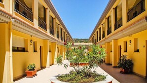 Un couloir aux murs jaunes, agrémenté de plantes en pot et doté d’un jardin central.