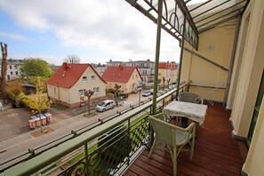 A balcony with a view of a street, a chair, and a table.