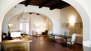 An interior with a reception desk, a dining area with a table and chairs, and a hallway with framed pictures on the walls. - Apartment in Tuscany with Pool near Florence (Rignano sull'Arno)
