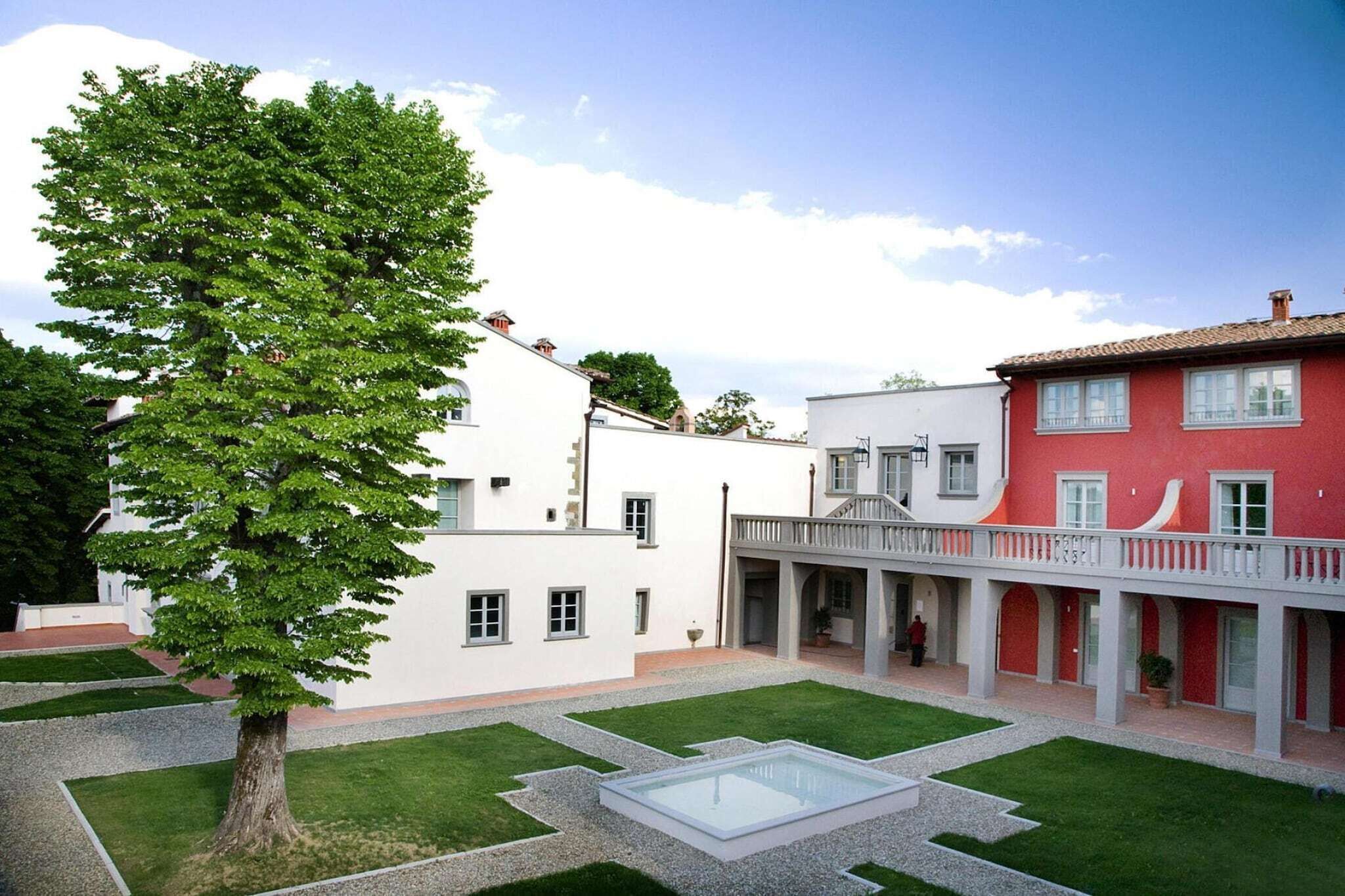 A courtyard with a large tree, a white building, and a red building with a balcony.