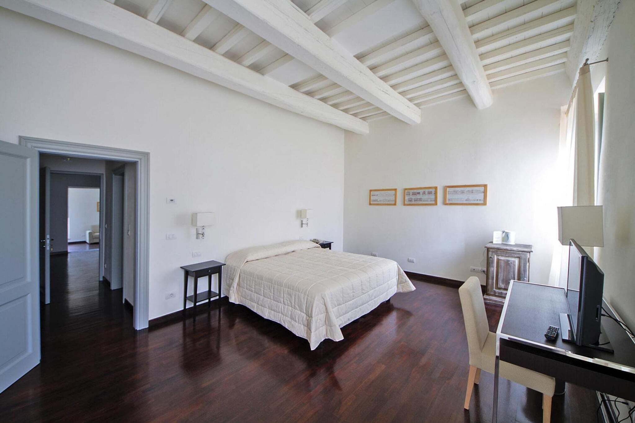 Un dormitorio con cama, escritorio, silla y computadora. Hay diplomas enmarcados en la pared.